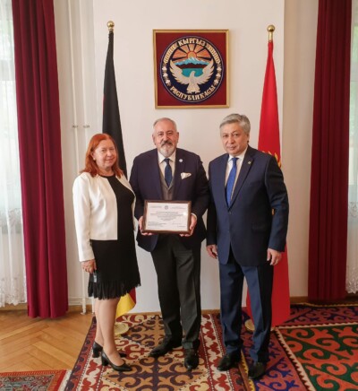 Moment wręczenia podziękowania za wieloletnie zaangażowanie się Konsula Janusza Krzywoszyńskiego na rzecz Republiki Kirgiskiej i jej obywateli. Moment wręczenia podziękowania za wieloletnie zaangażowanie się Konsula Janusza Krzywoszyńskiego na rzecz Republiki Kirgiskiej i jej obywateli.